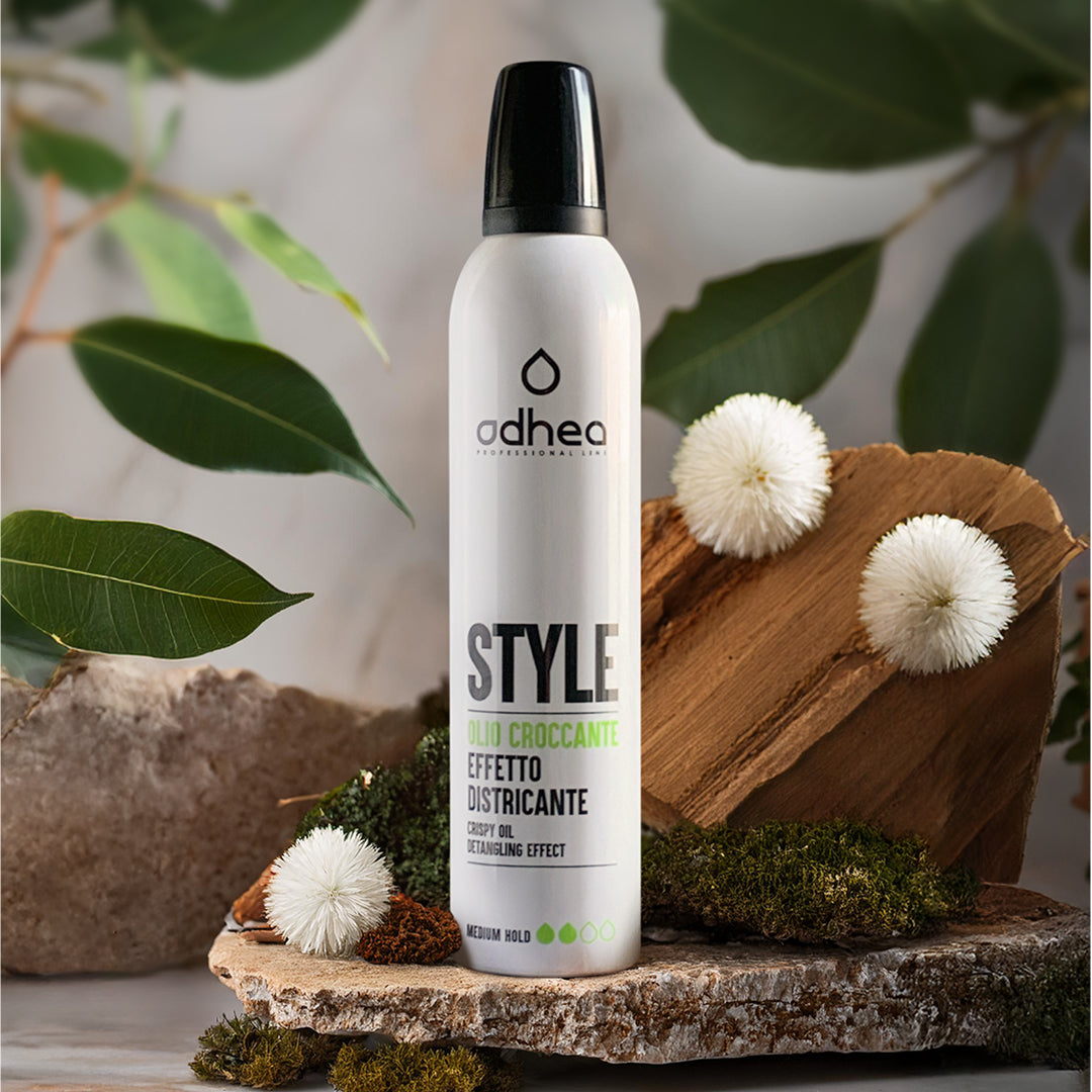 flacone bianco appoggiato in una ciocca di legno con del muschio intorno e dei fiori bianchi