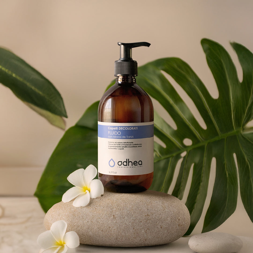 flacone marrone, appoggiato su un sasso bianco ovale, con due petali di fiori bianchi, dietro al sasso un ramo di foglia