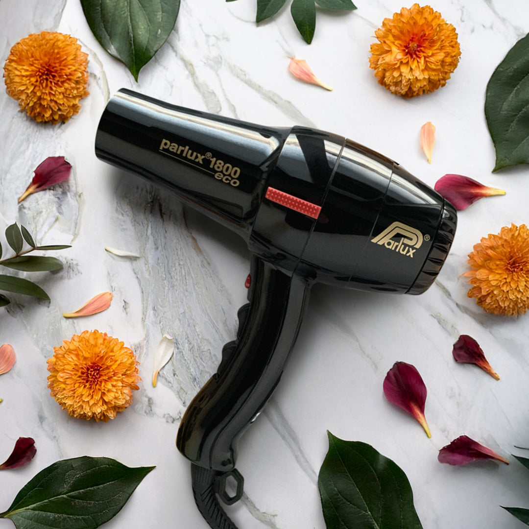 phon nero lucido che poggia su uno sfondo in marmo bianco con delle venature grigie, con attorno dei petali fucsia, arancio e delle foglie verdi