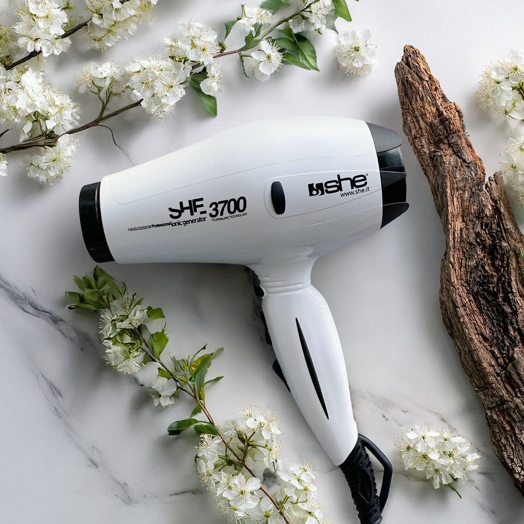 phon bianco lucido che poggia su uno sfondo di marmo bianco con delle venature grigie con attorno un pezzo di tronco e dei fiori bianchi