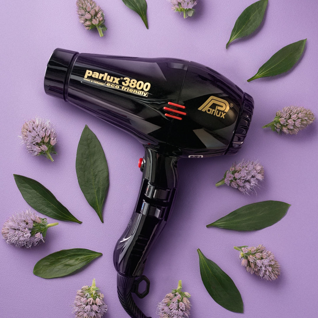 Phon Parlux, nero lucido, che poggia su uno sfondo lilla intenso e attorno ci sono delle foglie verdi e dei fiori lilla