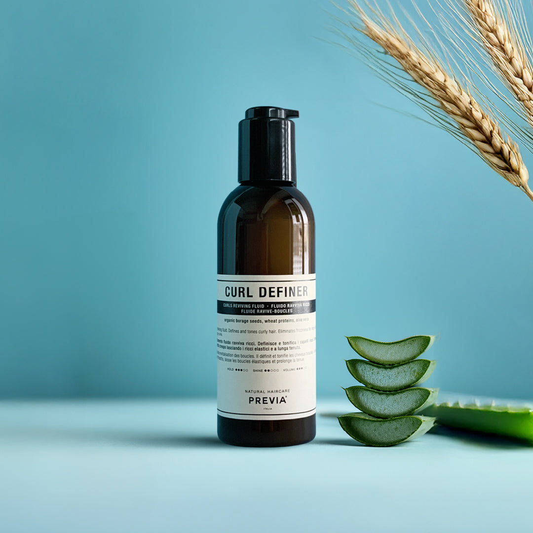 flacone del fluido rarriva ricci previa su sfondo azzurro con a sinistra delle foglie di Aloe e delle spighe di grano che fuoriescono