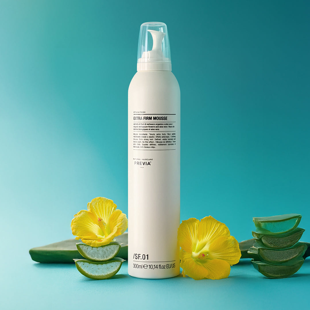 flacone mousse definizione previa su sfondo azzurro accerchiata da foglie di aloe fiori gialli