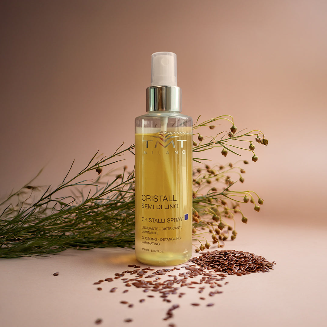 Prodotto TMT cristalli spray lucidanti su sfondo nuetro aranciato e il flacone poggia sui semi di lino