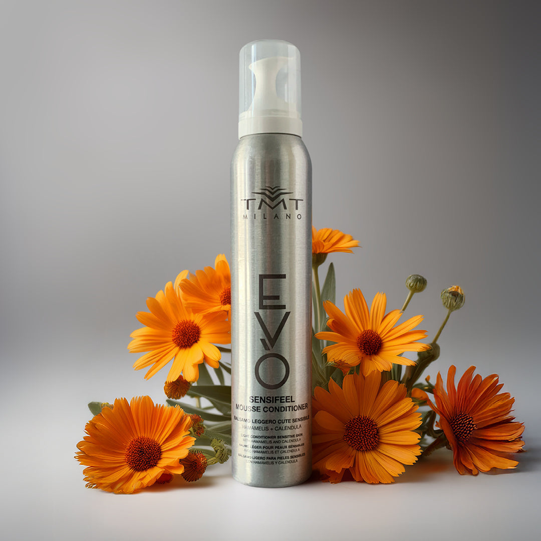 Flacone Evo Mousse Lenitivo su sfondo neutro grigio con attorno fiori arancio