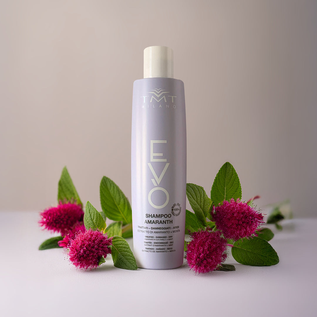 Flacone Evo Shampoo Amaranth di Tmt che poggia su sfondo neutro bianco - grigio con attorno dei fiori fucsia