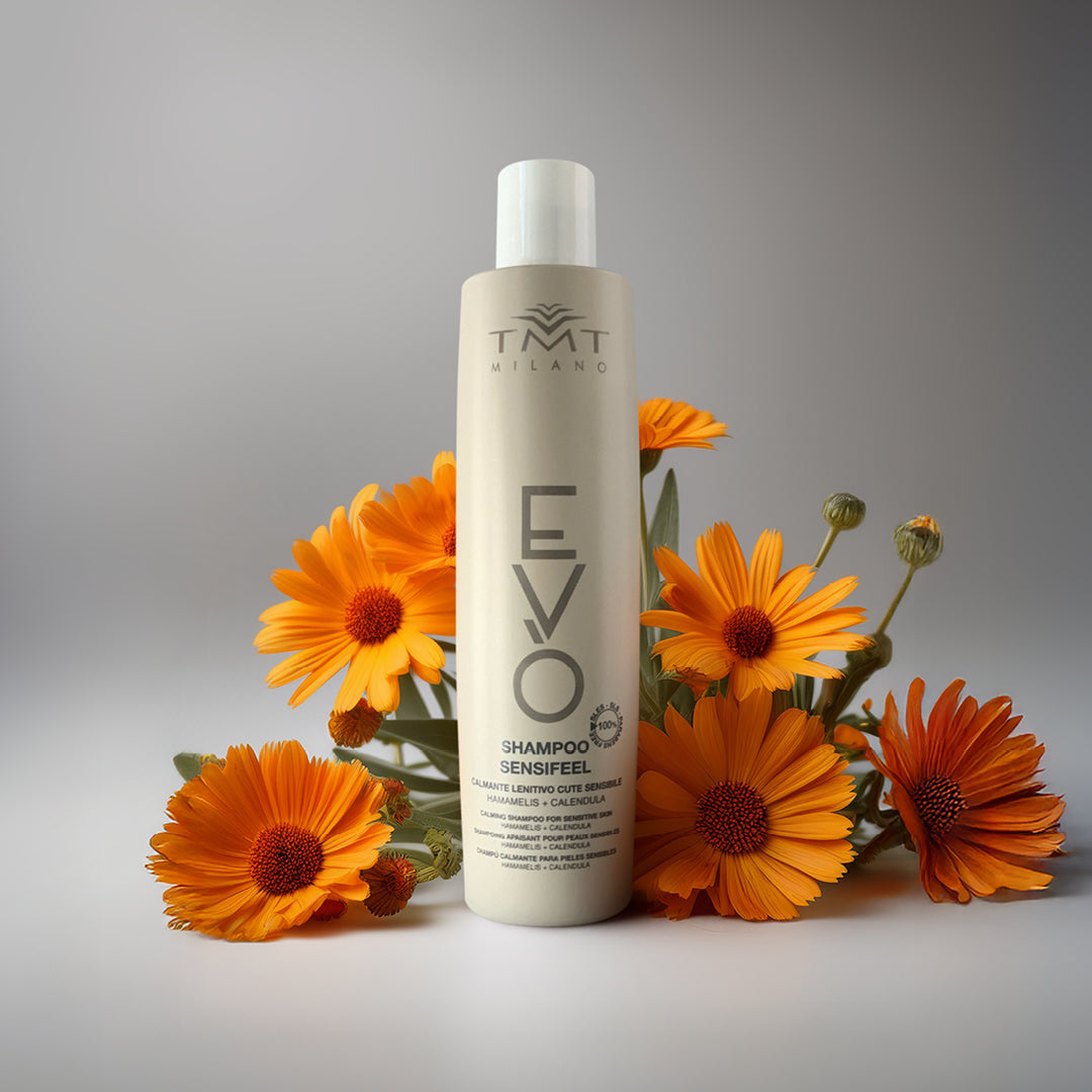 Flacone Evo Shampoo Lenitivo su sfondo neutro grigio con attorno fiori arancio