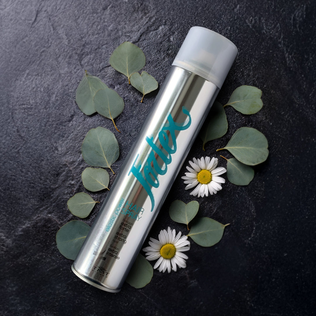 flacone hair spray di Fortex che poggia su uno sfondo grigio con attorno delle margherite