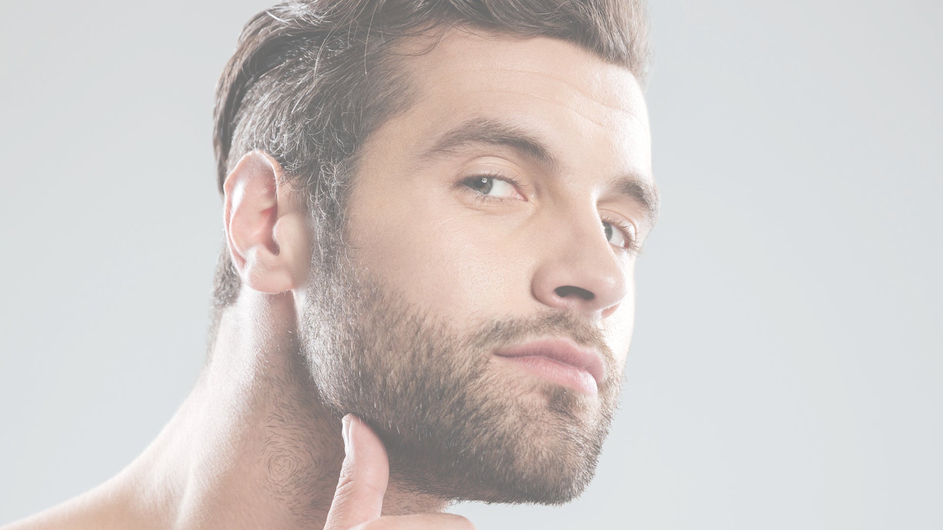 volto di un uomo giovane, moro di capelli che si tocca con il pollice la barba ben curata