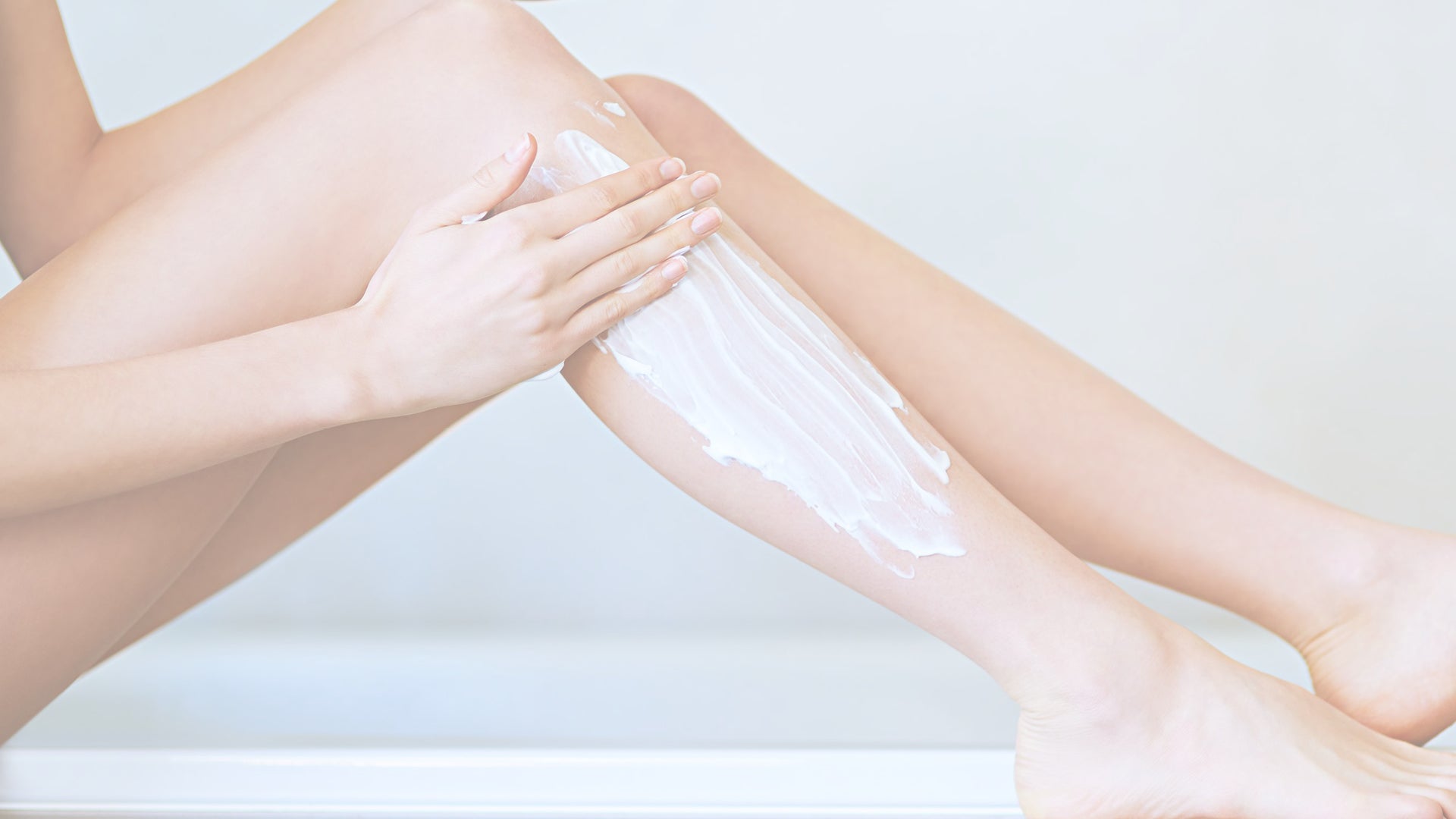 gambe di una donna mentre si spalma la crema nel polpaccio