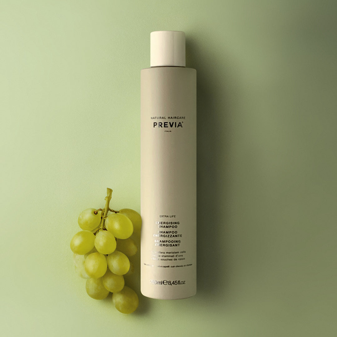 shampoo energizzante di previa su sfondo verde limone con uva verde che poggia alla destra del flacone