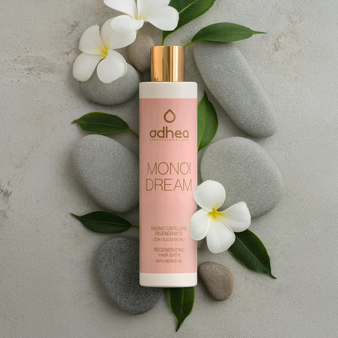 Flacone rosa su sfondo grigio sfumato. Attorno sassi di diversa grandezza, ovali e grigi, petali di fiori bianchi