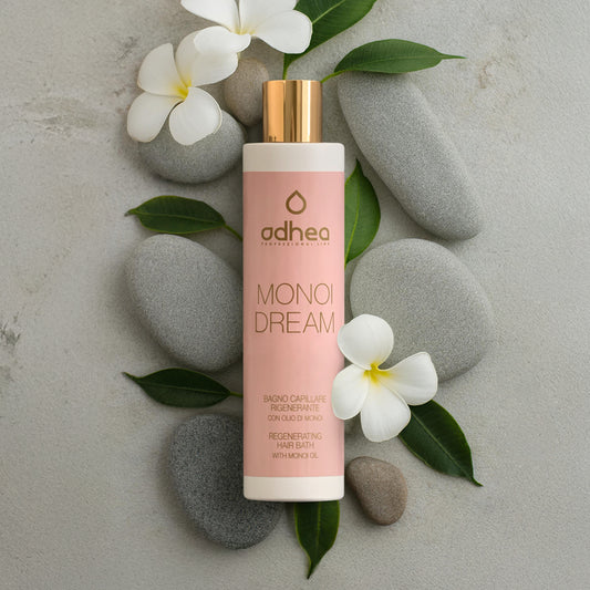 Flacone rosa su sfondo grigio sfumato. Attorno sassi di diversa grandezza, ovali e grigi, petali di fiori bianchi