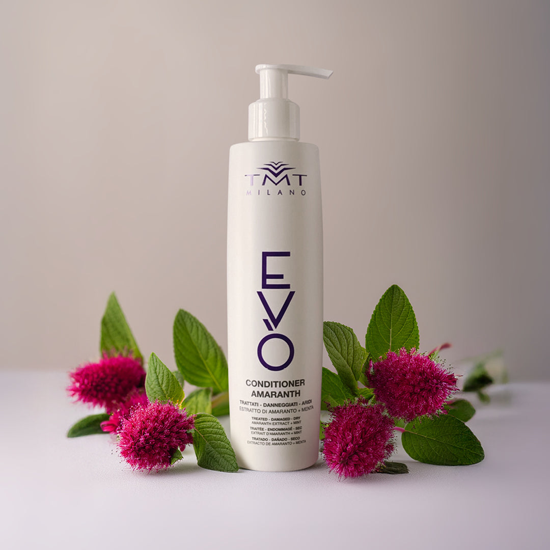 Flacone Evo Conditioner Amaranth di Tmt che poggia su sfondo neutro bianco - grigio con attorno dei fiori fucsia