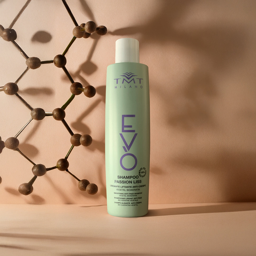 Flacone Evo Shampoo Lisciante su sfondo neutro grigio aranciato con una struttura di palline in legno