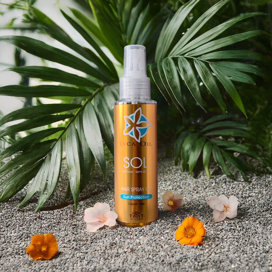 Prodotto Tmt Inca Oil che è uno spray protettivo che poggia su dei sassi grigi molto piccoli, dietro una piante verde e attorno dei fiori arancio