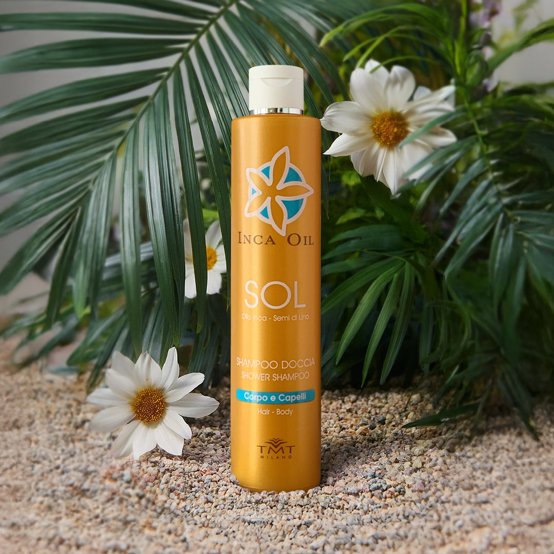 Prodotto Tmt Inca Oil che è uno shampoo corpo e capelli protettivo che poggia su dei sassi grigi molto piccoli, dietro una piante verde e attorno dei fiori arancio