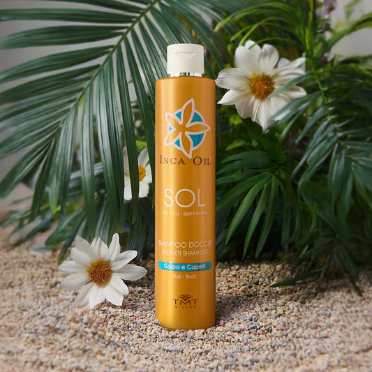 Prodotto Tmt Inca Oil che è uno shampoo corpo e capelli protettivo che poggia su dei sassi grigi molto piccoli, dietro una piante verde e attorno dei fiori arancio
