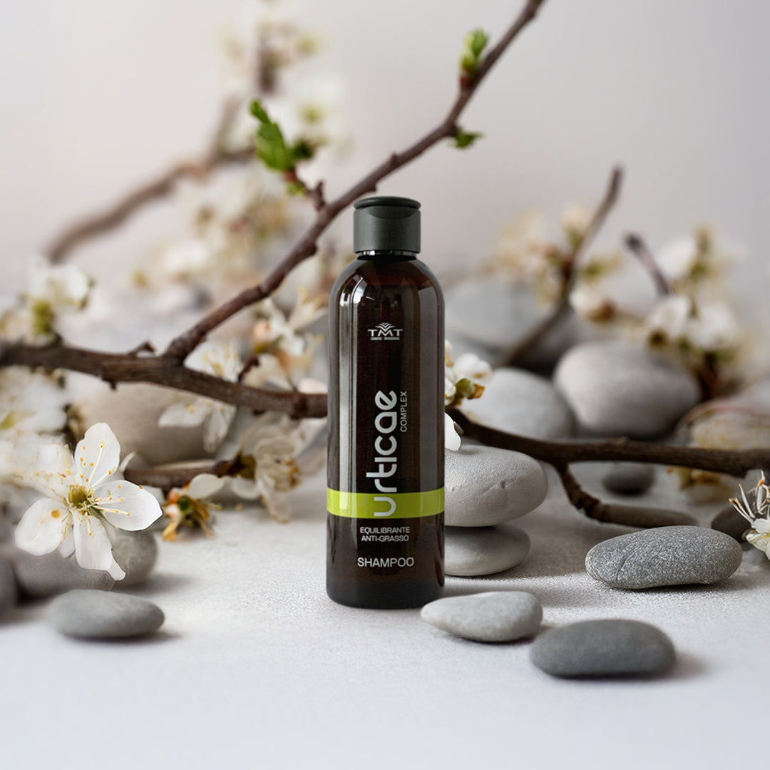 Prodotto Tmt Shampoo anti - grasso su sfondo con ramo di magnolia e sassi grigi piatti di varie dimensionei